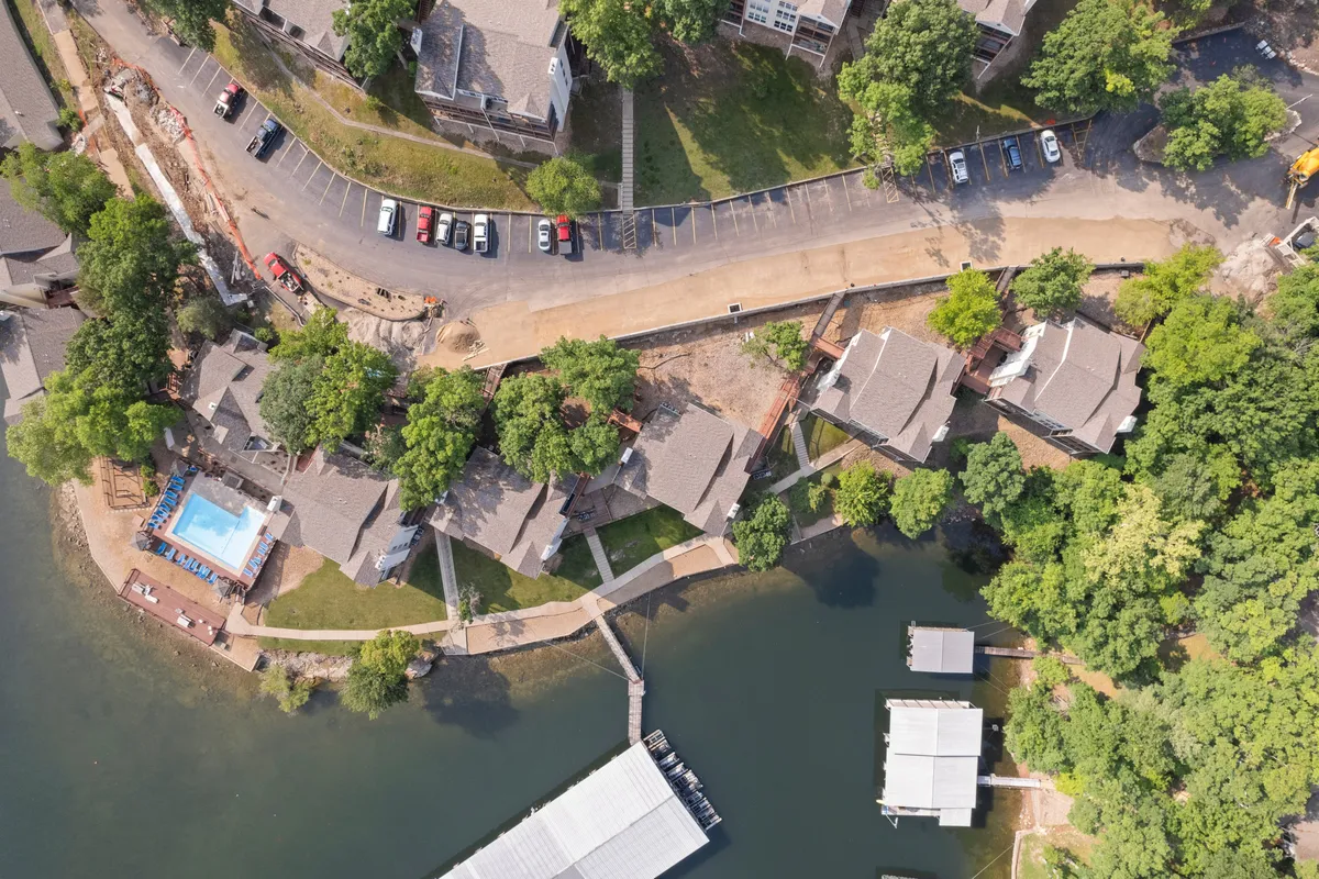 A broad view of the community’s swimming pool nestled beside the lake, with docks, lush green trees, and a road and parking area visible nearby. The image captures both the aquatic amenities and the immediate lakefront environment, suggesting easy transitions from poolside fun to lakeside adventures.
