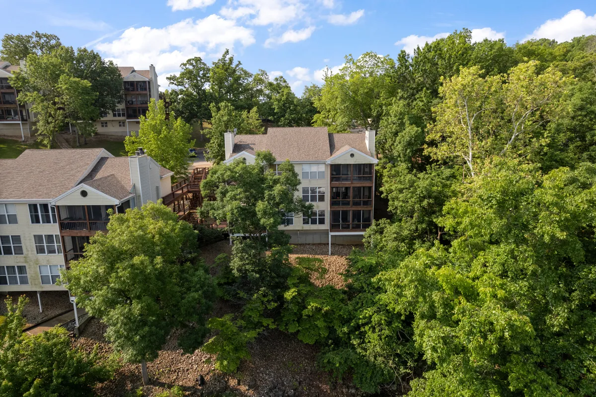 A peaceful exterior scene showing three residential buildings surrounded by lush greenery and connected by wooden walkways. The area invites residents to enjoy morning strolls, nature walks, and community gatherings amid a serene landscape.