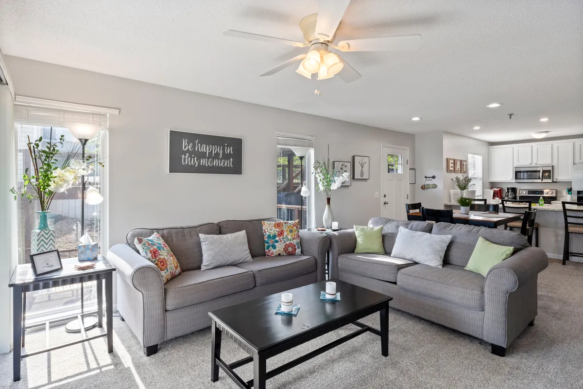 This image provides a warm and welcoming view of the open-plan living area. Sofas and a coffee table invite relaxation, while decorative wall art and a glimpse of the adjacent kitchen area add a homely touch. The space feels airy and ideal for conversation or winding down after a busy day.