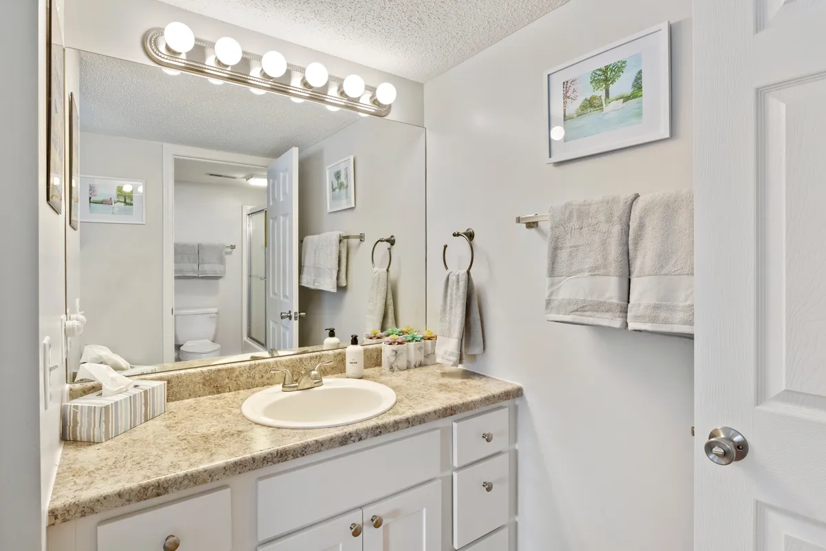 A modern bathroom featuring a spacious vanity with a sink, large mirror, decorative artwork, and neatly arranged towels. The room is bright, clean, and inviting, suggesting a spa-like experience.