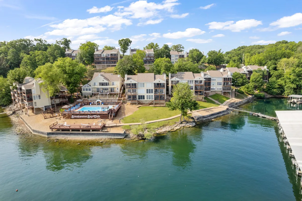 This image displays a vibrant community swimming pool set against a waterfront backdrop, with landscaped grounds and residential buildings visible nearby. Sunbathers and swimmers enjoy the inviting atmosphere, while the setting sun casts a warm glow over the scene, enhancing the tranquil mood.
