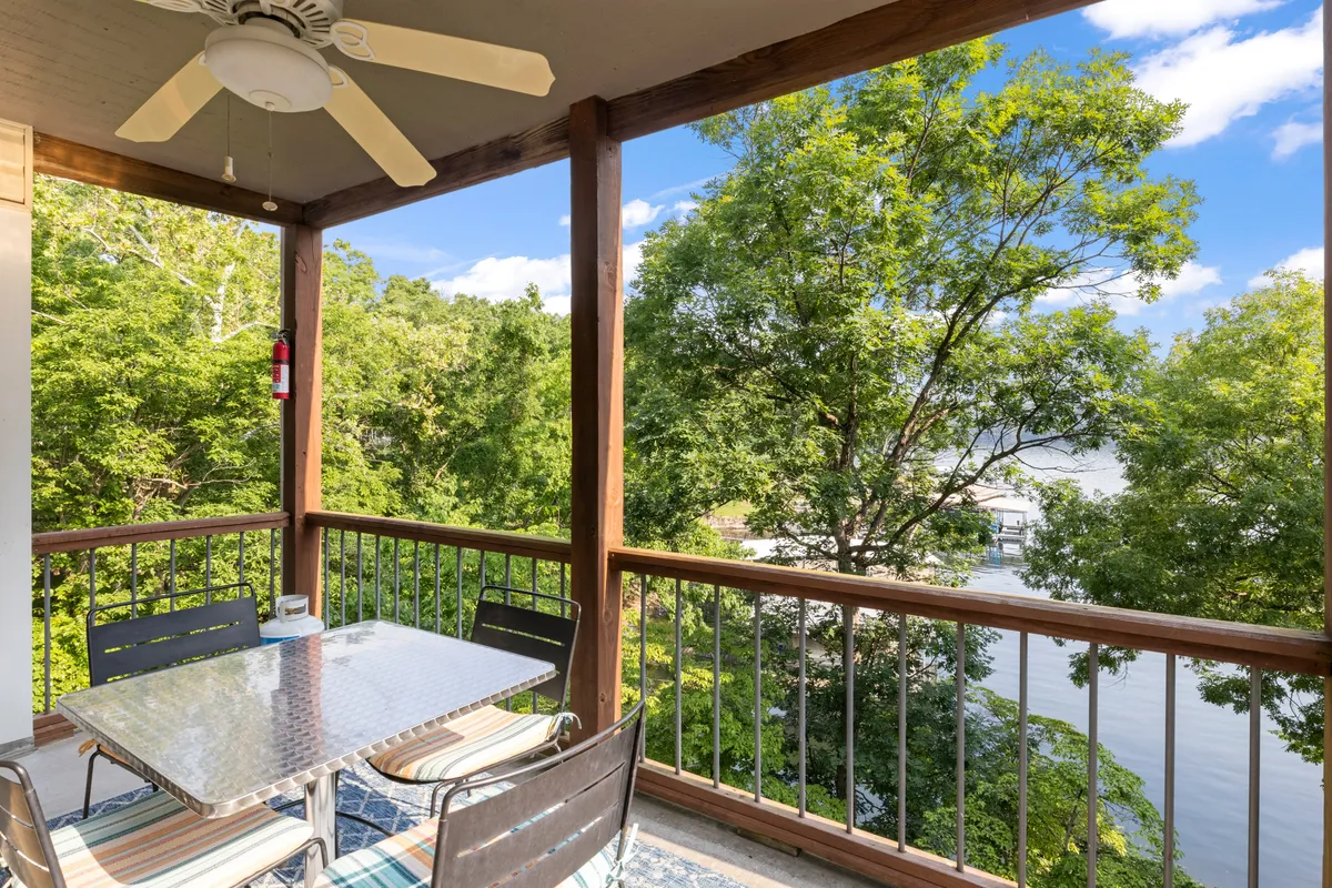 A tranquil outdoor dining area with a table and chairs, ceiling fan overhead, and scenic water view framed by green trees. The scene captures the inviting atmosphere of outdoor living, perfect for lakeside picnics, gentle strolls, or simply enjoying nature with family.