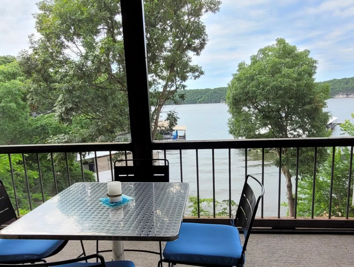 A serene outdoor dining area overlooking the lake, with an inviting table and chairs framed by lush greenery. The setting is peaceful and perfect for al fresco meals, with views of the water and nature beyond.