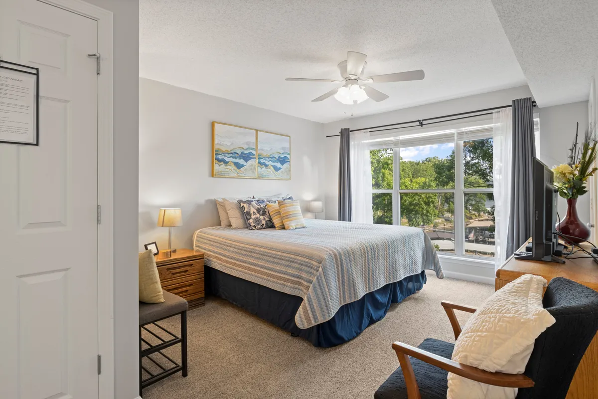 A serene bedroom with a comfortable bed, window, and artwork, filled with natural sunlight. The inviting atmosphere encourages rest and relaxation, while the window offers a visual connection to the outdoors.