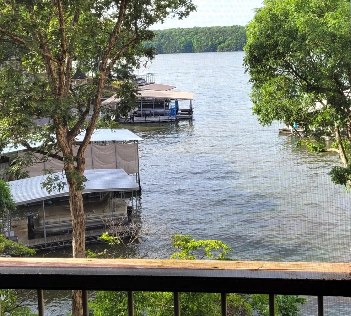 The image showcases a tranquil lakeside view with calm water, private docking structures, and lush green surroundings. The scene exudes serenity, with the promise of sunset vistas, opportunities for boating or fishing, and inviting spaces for relaxing by the water's edge.