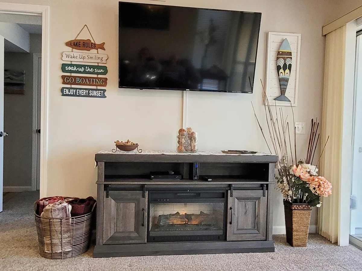 A cozy and inviting living space highlighted by a fireplace, television, and decorative touches, with a patio door visible that leads to an outdoor area—ideal for enjoying sunsets or gathering with family during any season.