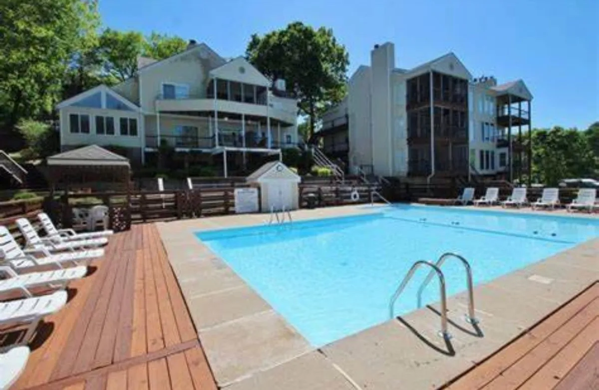 This exterior scene centers on a sparkling swimming pool surrounded by a deck area, green trees, and neighboring buildings. The poolside area exudes a relaxed, cheerful mood, ideal for breaks or socializing after a productive day.