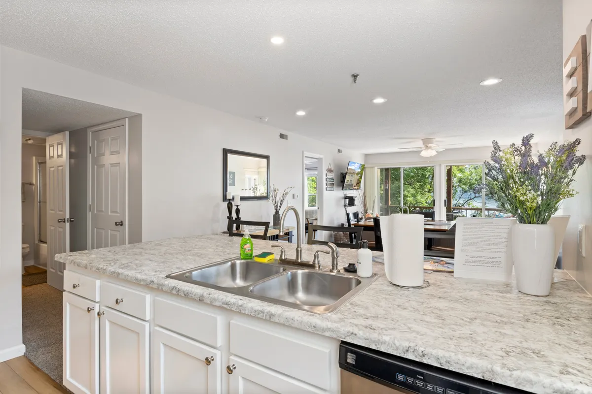 A broad view of the kitchen and dining area, emphasizing the kitchen island, adjacent sink, lavender flowers, and the connected dining space with open windows. The layout is open and airy, ideal for cooking and entertaining.