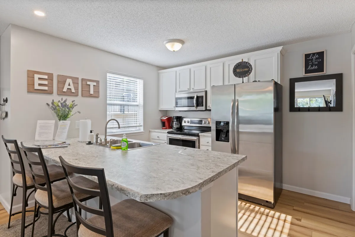 A bright, inviting kitchen space featuring a spacious island countertop, stainless steel appliances, and wooden letters spelling 'EAT' on the wall. A vase of fresh flowers adds a homey, welcoming feel. The layout encourages group cooking and socializing.