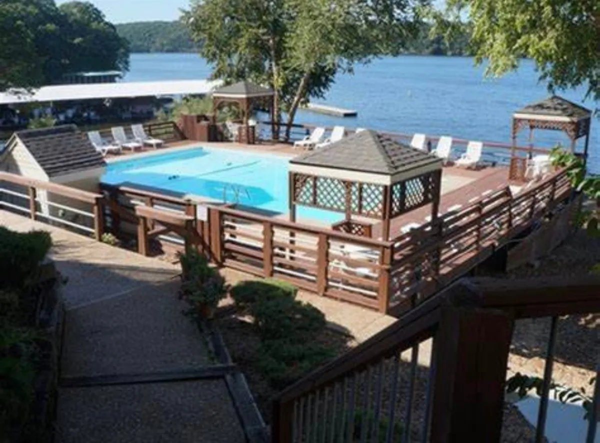 An inviting pool area featuring a gazeebo, deck chairs, and a stunning lake view. The scene is perfect for both socializing and quiet relaxation, as the lake sparkles beyond the pool and the gazeebo provides a shaded retreat.